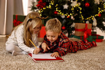 Little kids writing letter to Santa Claus on floor at home. Christmas celebration