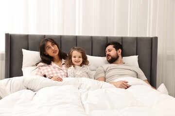 Fototapeta premium Happy playful daughter with her overwhelmed parents in bed at home