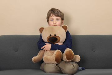 Autism concept. Lonely little boy with teddy bear on sofa at home
