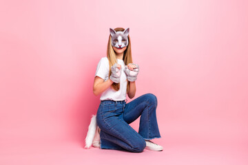 Young girl wearing a cat mask kneeling on a pink background, showcasing playful fashion and cosplay...