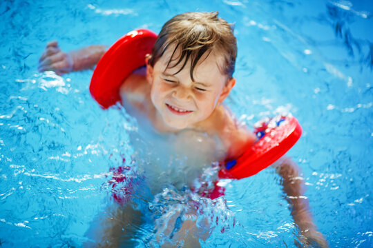 Active adorable little preschool kid boy with swimmies learning to swim in an indoor pool. Active and fit leisure for children. Happy child making sports and learning safe swimming.