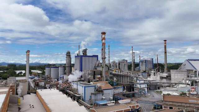 V&iacute;deo com vis&atilde;o a&eacute;rea de chamin&eacute;s e caldeiras de uma ind&uacute;stria de papel e celulose em um dia ensolarado, destacando o processo de produ&ccedil;&atilde;o e a emiss&atilde;o de vapor na f&aacute;brica