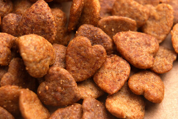 Dry heart shaped pet food on brown background. Pile of ready-to-eat cat feed