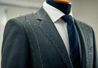 Tailored suit displayed on mannequin with visible stitching and pins highlighting craftsmanship