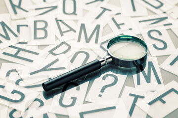 A magfiying glass placed on the pile of English alphabets plastic plates with a question mark sign, glossary and communication concept