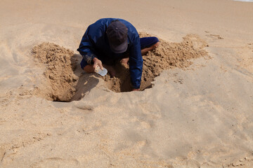 A man by the sea digs a hole in the sand in search of treasure