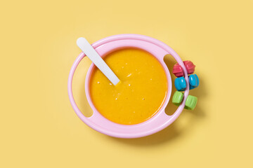 Bowl with baby food. vegetable puree on yellow background. Top view