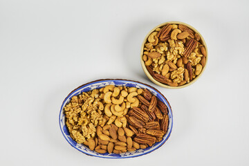 Assorted nuts in a stoneware container with a straw basket, on a white background. Almonds, Walnuts, Cashews and Chestnuts