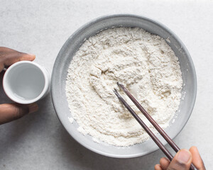 Overhead view of noodle dough being being mixed in a grey bowl, top view of flour and water being mixed, process of making hand pulled noodles