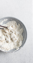 Overhead view of noodle dough being being mixed in a grey bowl, top view of flour and water being mixed, process of making hand pulled noodles
