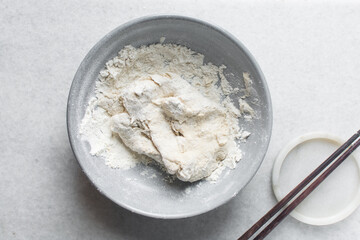 Overhead view of noodle dough being being mixed in a grey bowl, top view of flour and water being mixed, process of making hand pulled noodles