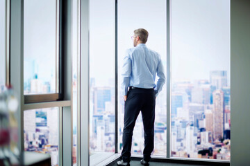 Rear view of a businessman standing in a modern office and looking out of over the city