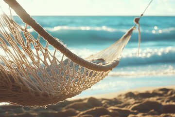 A close-up of a hammock hanging between two trees on a sandy beach with ocean waves in the background.