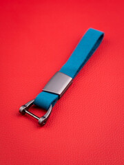 A close-up view of a sleek  blue  leather  keychain featuring metal accents against a red backdrop.