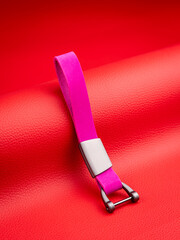 A close-up view of a sleek  pink  leather  keychain featuring metal accents against a red backdrop.