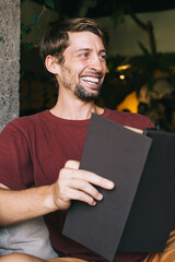 Cheerful emotional caucasian male laughing during reading stories enjoying recreation and hobby,...
