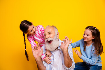 Smiling elderly man bonding with two young girls in casual attire on a vibrant yellow background,...