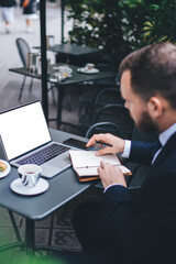 Male entrepreneur using mockup laptop for analyzing online investment connected to 4g internet in street cafe, experienced businessman browsing information on blank netbook with copy space area