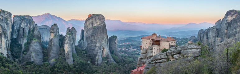 Sunset view of the Meteora monasteries in Greece, perched on towering rock formations, surrounded by a stunning mountainous landscape.