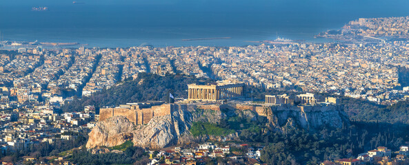 A panoramic view of Athens, Greece, featuring the Acropolis with the Parthenon temple, surrounded by the dense cityscape and the Aegean Sea in the background.