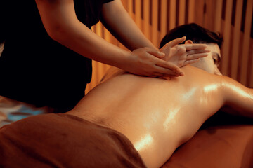 Caucasian man customer enjoying relaxing anti-stress spa massage and pampering with beauty skin recreation leisure in warm candle lighting ambient salon spa at luxury resort or hotel. Quiescent