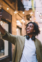 Handsome caucasian male in trendy casual wear exploring historical center in city posing for selfie on smartphone camera, positive curly man blogger influencer shooting video on mobile phone for share