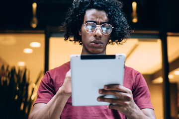 Frowning man in eyeglasses browsing tablet