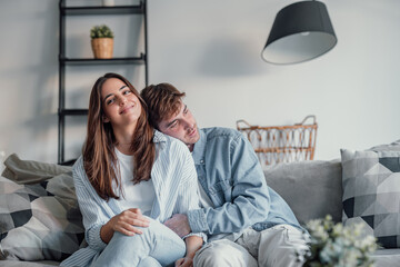 Portrait of young 20s just married couple in love posing photo shooting seated on couch in modern...