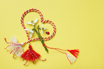 Heart made of red and white cord, snowdrop flowers on a yellow background, symbol of the holiday Martenitsa March 1, Martisor, Baba Marta, copy space