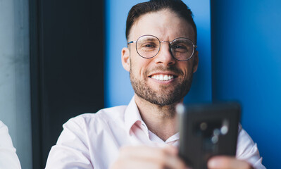 Half length portrait of cheerful male blogger in eyewear smiling at camera while creating web...