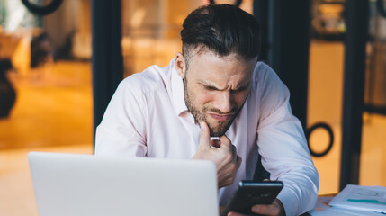 Puzzled male freelancer checking received email on smartphone gadget during remote job in...