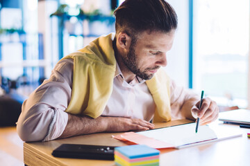 Naklejka premium Smart casual male entrepreneur drawing with stylus analyzing financial exchange of bitcoin during remote job with money investment, Caucasian man 30s with electronic pen working on freelance