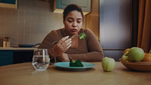 Upset overweight woman eats broccoli feeling disgust to food