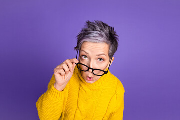 Surprised woman with glasses in yellow sweater against purple background