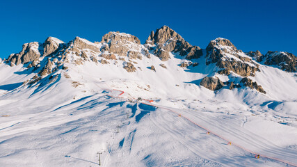 Aerial breathtaking view of touristic ski resort surrounded by high snow covered mountains peaks,...