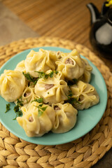 A plate of freshly steamed dumplings garnished with herbs, served with a black teapot and chopsticks on a rustic table setting. Mongolian Food: Buuz (Steamed Mongolian Dumplings)