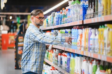 Portrait of focused man buying household chemicals in supermarket, reading labels on bottles