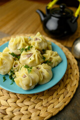 A plate of freshly steamed dumplings garnished with herbs, served with a black teapot and chopsticks on a rustic table setting. Mongolian Food: Buuz (Steamed Mongolian Dumplings)