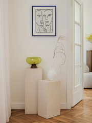A corner of the room adorned with a textured pedestal display. A bold green glass lamp and a white...