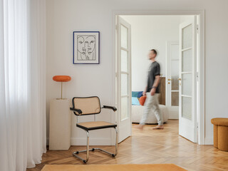 A living space with a rattan and chrome chair, complemented by an orange lamp and abstract art. The...