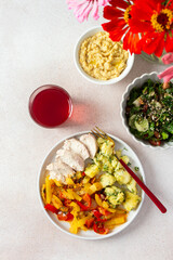 A balanced meal of boiled potatoes with baked vegetables and chicken breast, paired with a fresh tomato and cucumber salad topped with seeds, and a refreshing raspberry compote