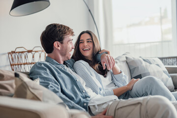 Portrait of young 20s just married couple in love posing photo shooting seated on couch in modern...