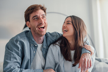 Portrait of young 20s just married couple in love posing photo shooting seated on couch in modern studio apartments, concept of capture happy moment, harmonic relationships, care and sincere feelings.