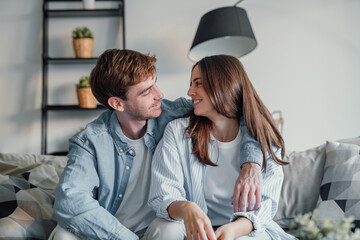 Portrait of young 20s just married couple in love posing photo shooting seated on couch in modern studio apartments, concept of capture happy moment, harmonic relationships, care and sincere feelings.