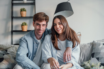Portrait of young 20s just married couple in love posing photo shooting seated on couch in modern...