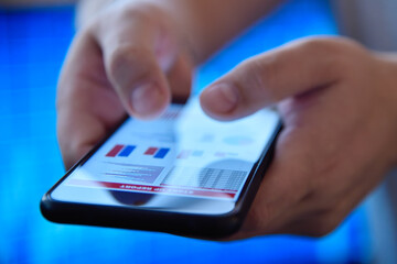 Hands using a mobile phone displaying financial charts
