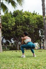 Brunette Woman Doing Squats on Grass in Park, Filming Herself with Mobile Phone
