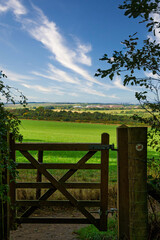 Fototapeta premium A rustic wooden gate opens to a picturesque landscape of rolling green fields and a bright blue sky, Harrogate, Yorkshire, UK.