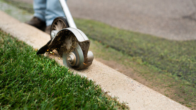 Landscape worker power edging green lawn next to curb.