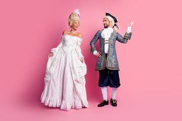 Young couple in historical royal attire posing with joy on a pink backdrop, embodying classic...